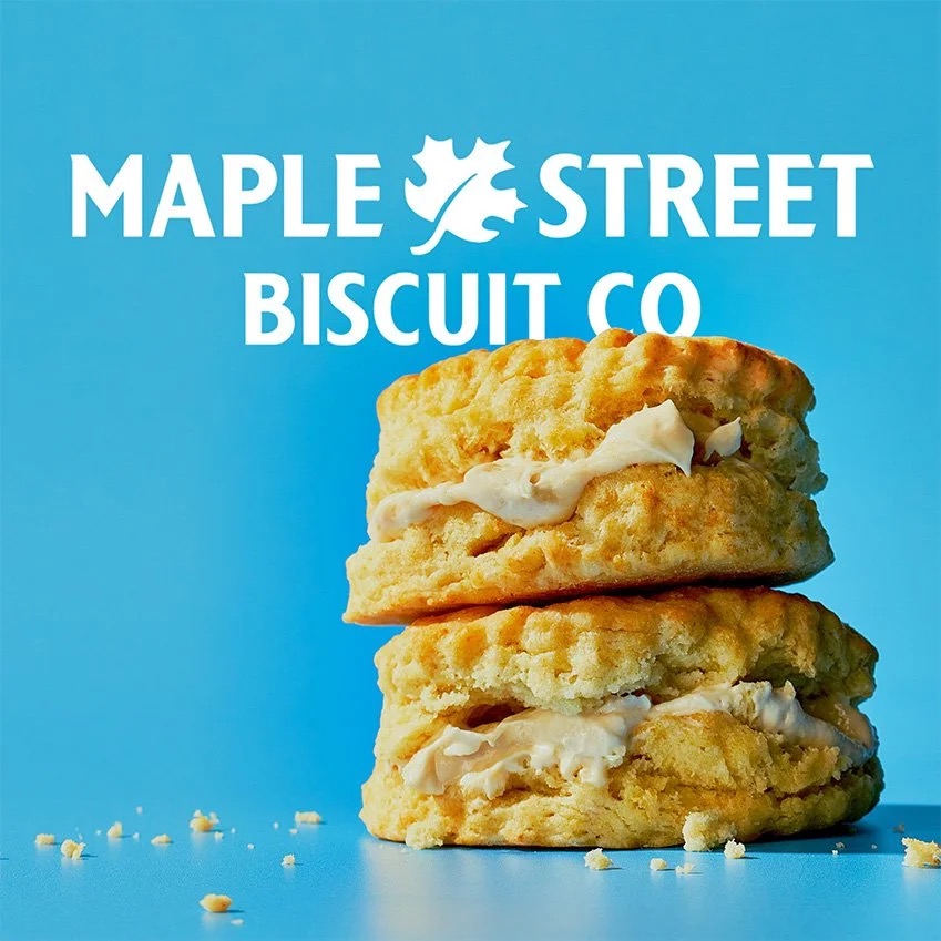 Two tall buttermilk biscuits split and spread with maple butter on a bright blue backdrop